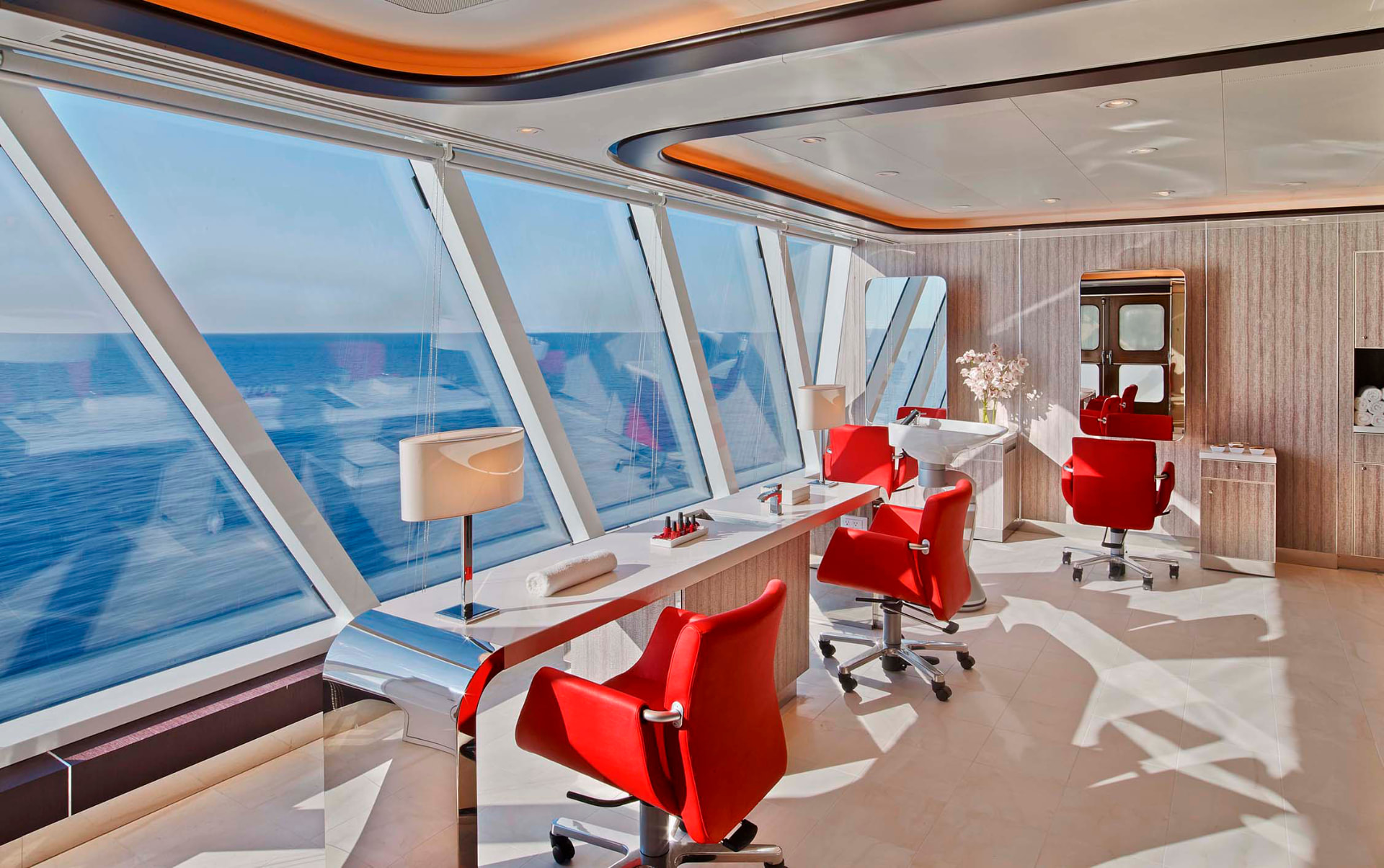 Kapsalon aan boord met rode stoelen en schuine ramen op zee