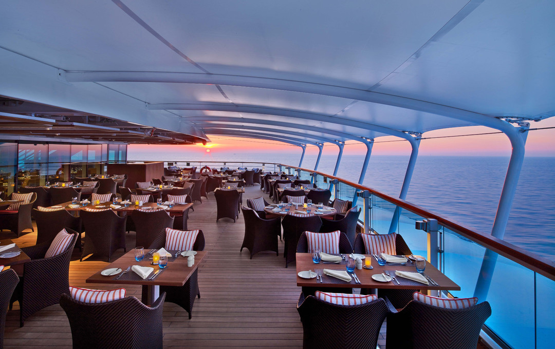 Restaurant op het buitendek met gedekte tafels en zonsondergang boven zee