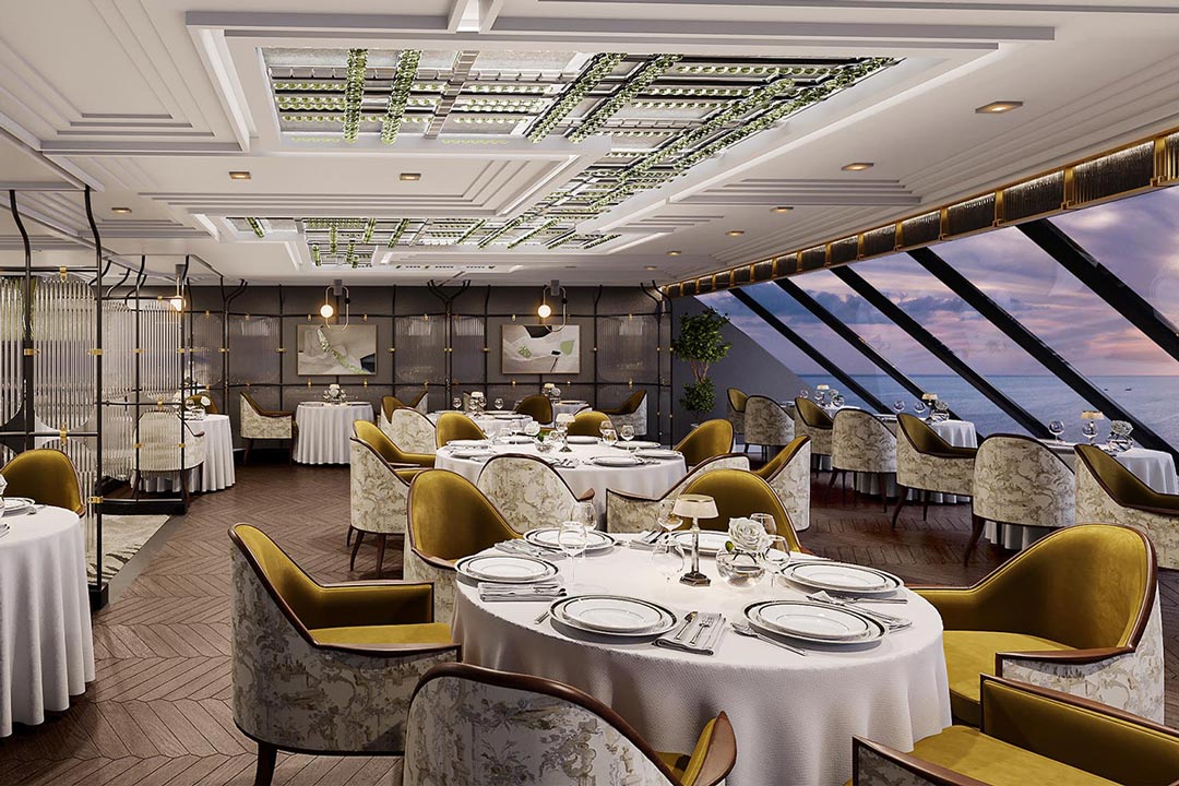 Restaurant aan boord met ronde gedekte tafels, okergele fauteuils en schuine panoramaramen