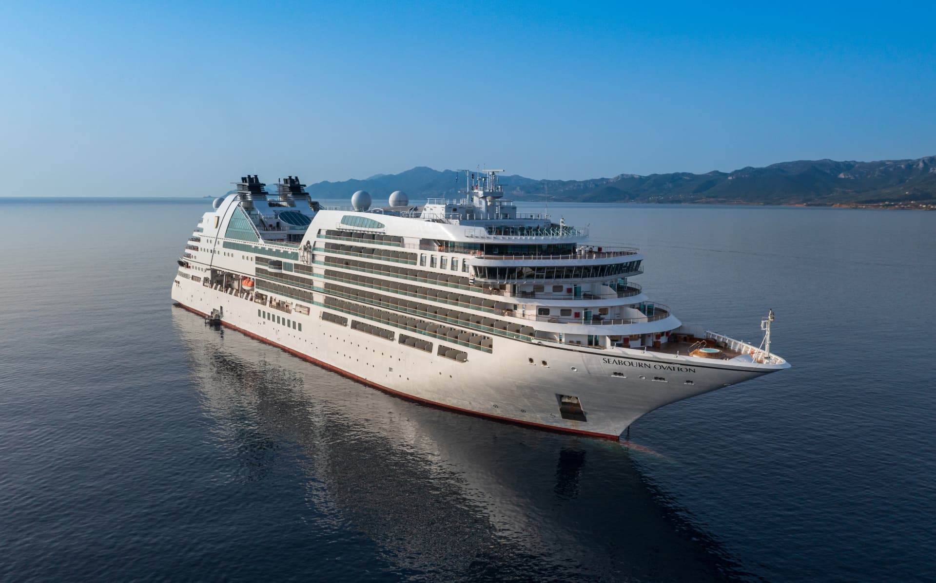 De Seabourn Ovation voor anker in kalme zee met bergen op de achtergrond